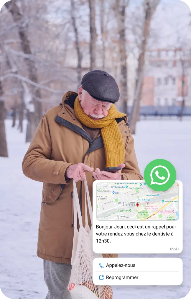 Un homme âgé, dans la neige, consulte son téléphone pour connaître l'emplacement via un message WhatsApp professionnel.